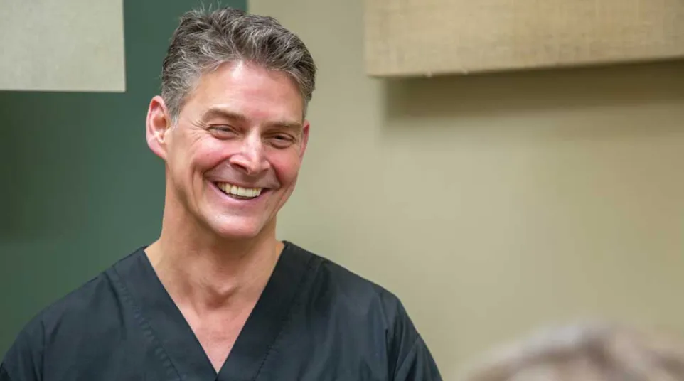 Smiling male healthcare professional in black scrubs interacting with a patient in a clinical setting