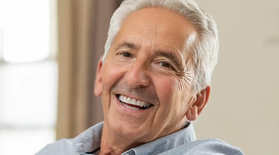 Smiling mature man with gray hair relaxing on a couch in a bright, comfortable room.
