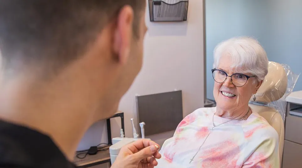 Dentist explaining dentures to elderly female patient in bright dental office with natural light.