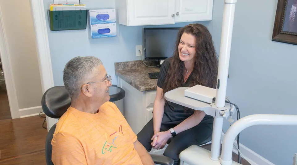 Dentist smiling and conversing with male patient in orange shirt at dental office during checkup.