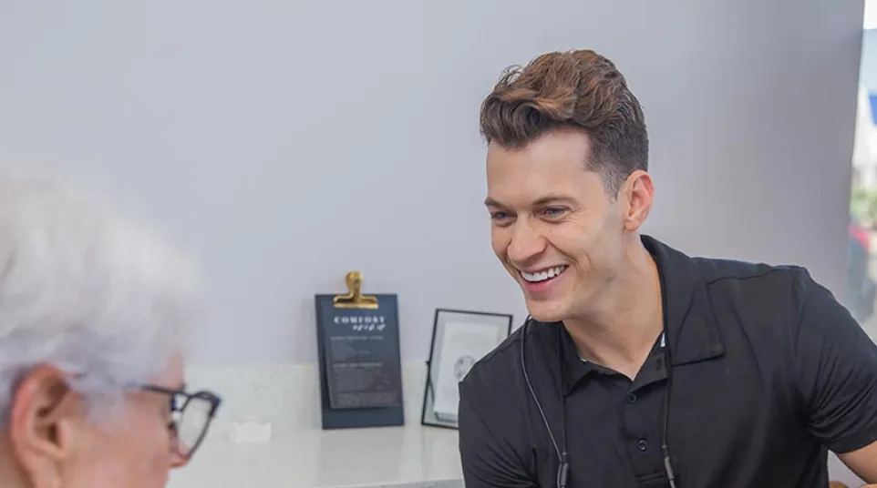 Female healthcare professional smiling while taking notes on clipboard during patient consultation in medical office.