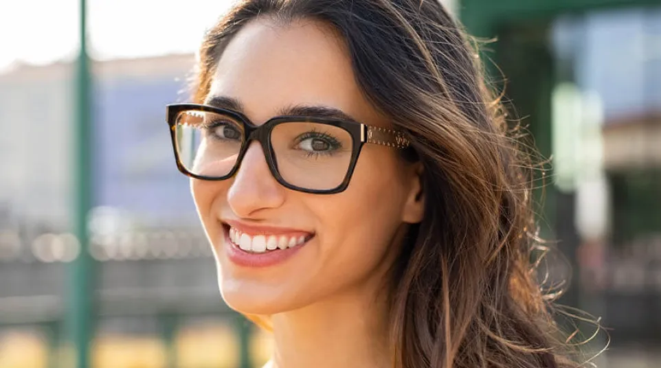 Smiling woman wearing glasses in a sunny outdoor setting, showcasing bright colors and casual style.