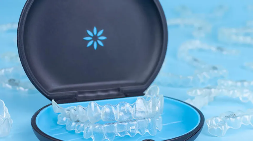 Clear dental aligners displayed in an open black and blue carrying case on a light blue background.