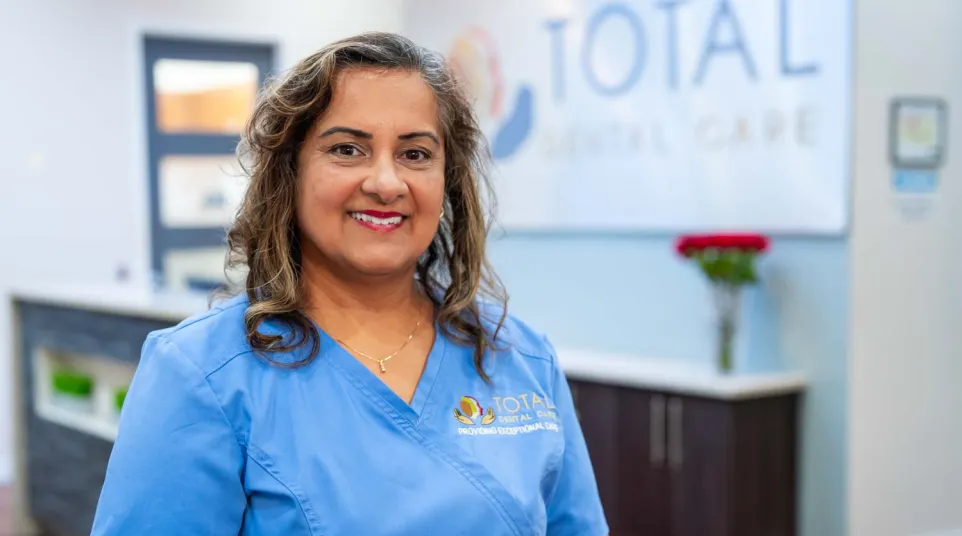 Smiling female dental professional in blue scrubs standing inside a modern dental clinic reception area.