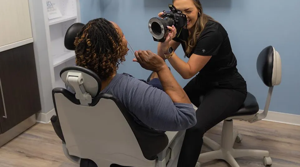 Dentist photographing patient’s teeth in dental office with teeth close-up image on screen.