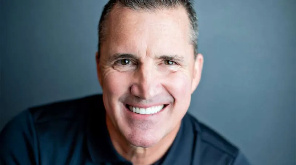 Smiling man in black Adidas polo shirt against plain gray background, close-up portrait with spiked hair.