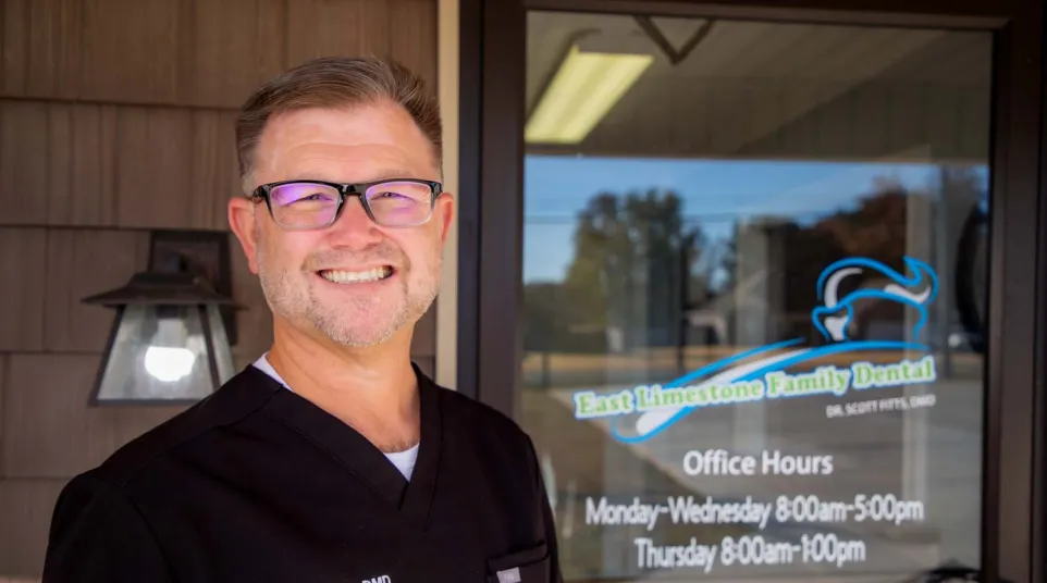 Smiling male dentist wearing glasses and black scrubs standing outside East Limestone Family Dental office.