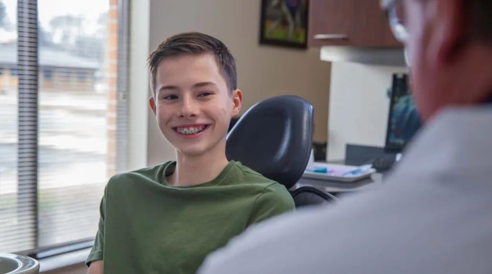 Smiling teenage boy with braces sitting in a dentist chair during a dental checkup in a modern clinic.