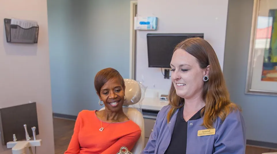 Two healthcare professionals in black scrubs smiling and discussing documents in a medical office.