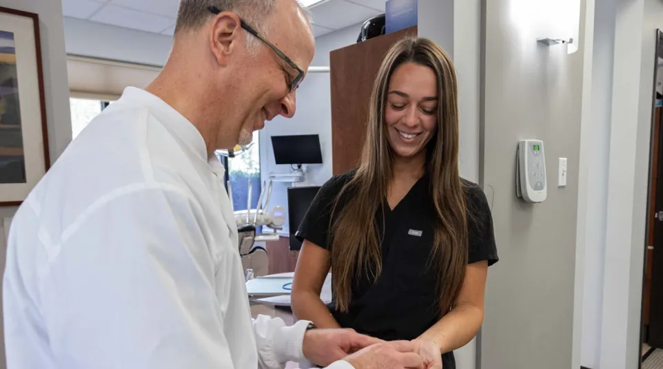 Dentist and dental assistant smiling and holding a dental mold in a modern clinic office.