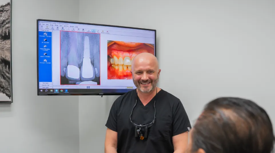 Dentist consulting patient with dental X-ray and teeth images displayed on screen in modern clinic