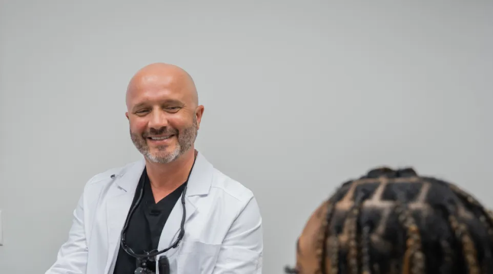 Dentist in white coat showing a dental mold to a patient with braided hair in a clinic setting.