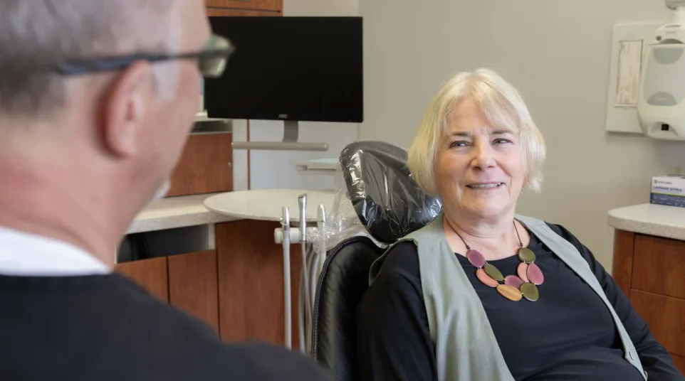 Senior woman smiling while sitting in dental chair talking to dentist in modern clinic.