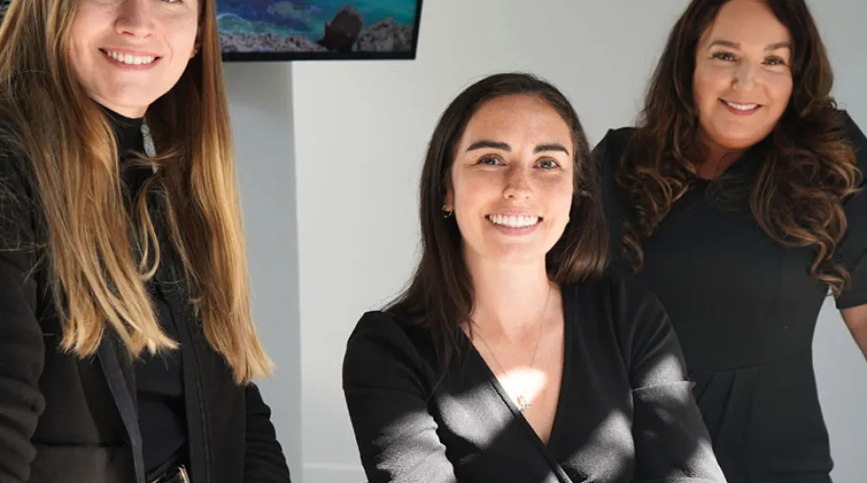 Three professional women smiling inside an office