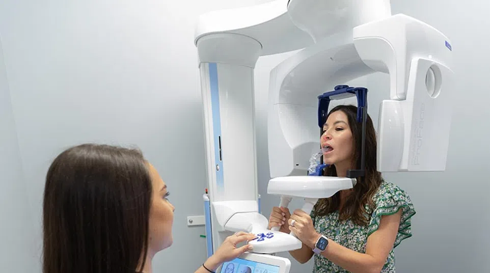 Woman undergoing a dental 3D X-ray scan with a technician operating the machine in a clinical room.