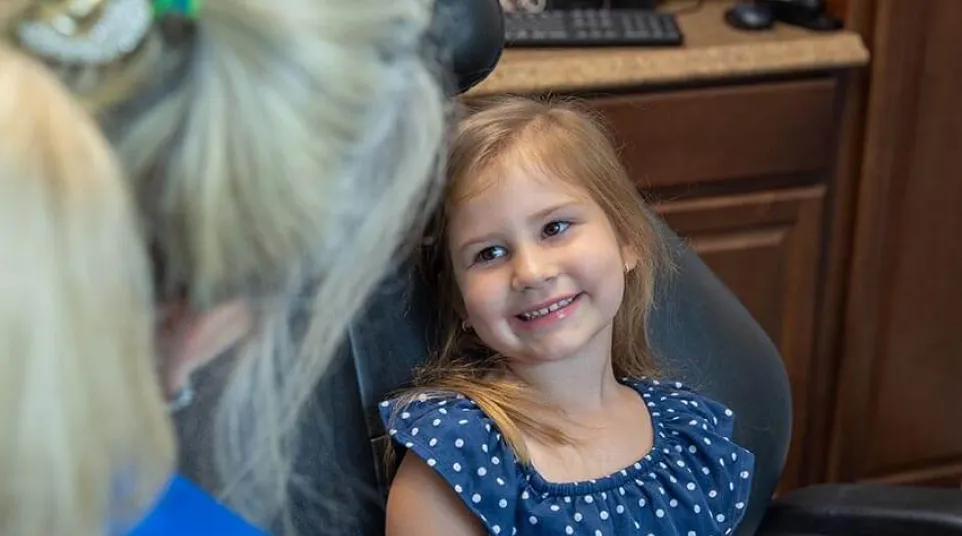 A young girl sitting at the dental chair smiles to a dental staff member