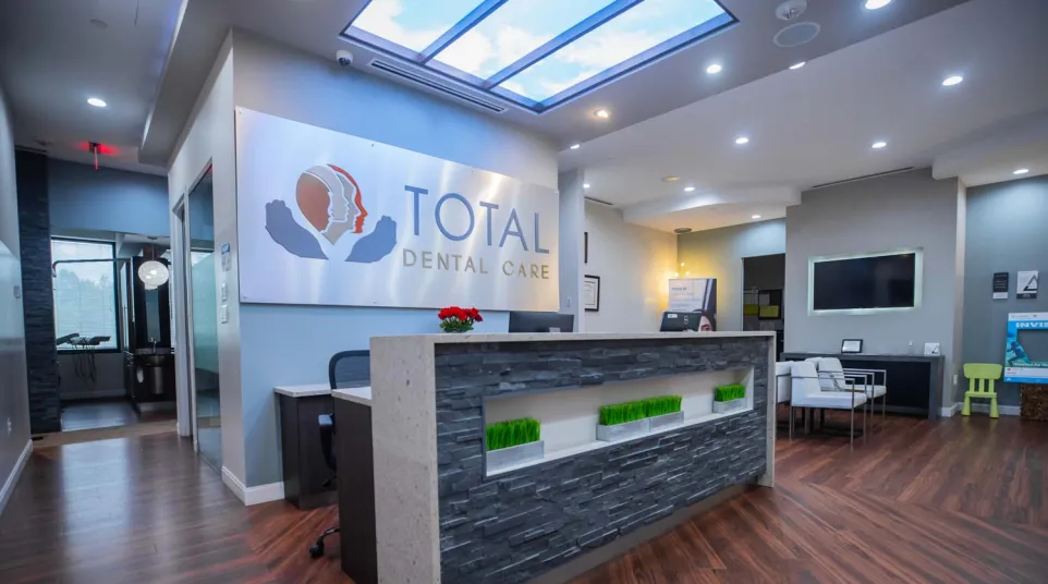 Modern dental office reception with stone desk, wood flooring, ceiling sky light, and Total Dental Care logo wall art.