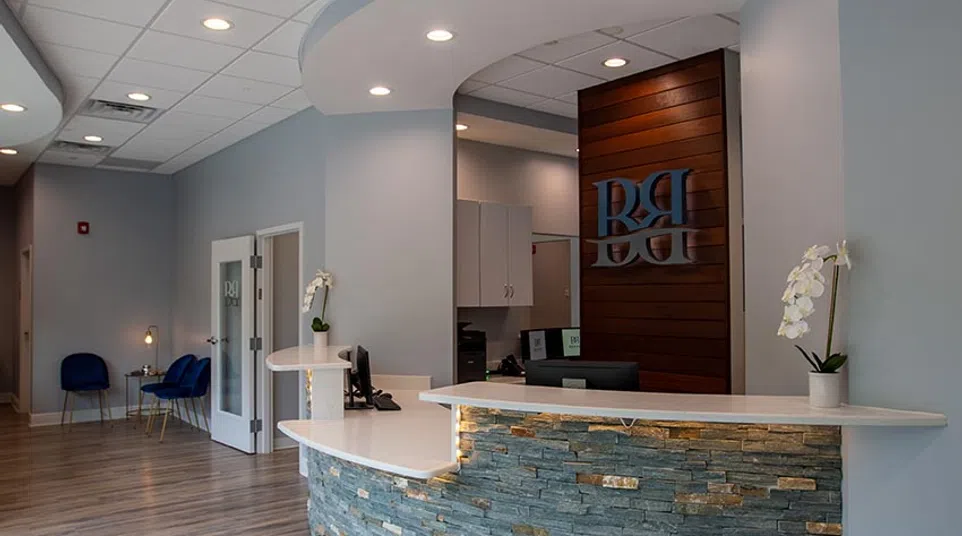 Modern medical office reception area with stone counter, wooden panel backdrop, and blue seating in waiting area.