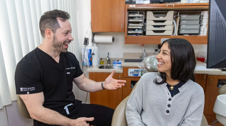 Dentist and patient smiling while discussing dental care in a bright, organized dental office.