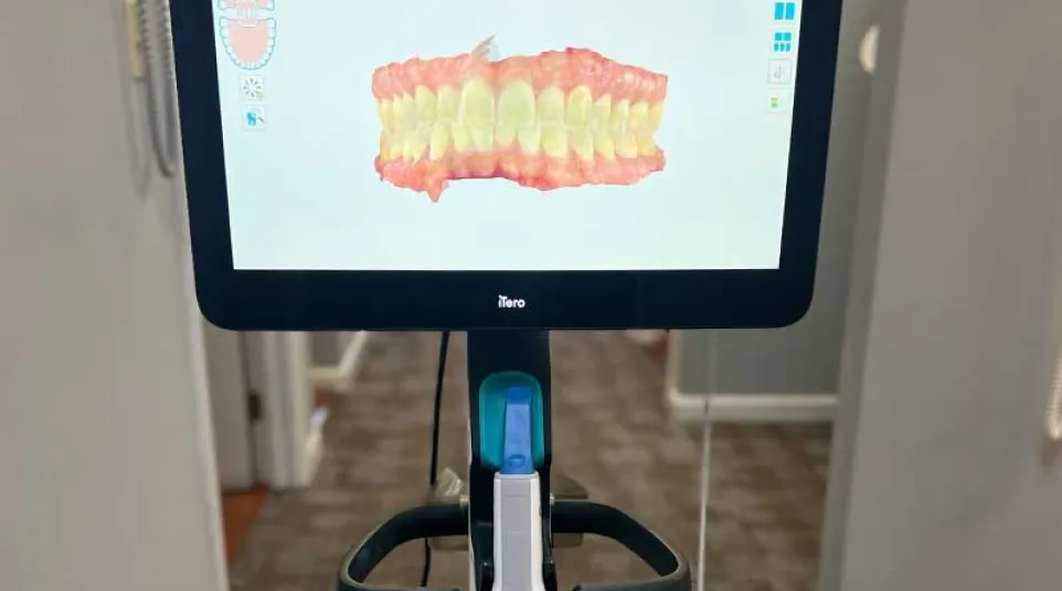 Dental imaging device displaying a 3D model of teeth and gums in a clinic setting.