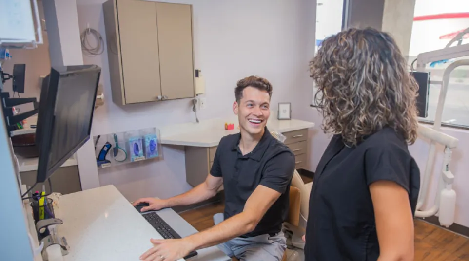 Dental office staff smiling and interacting at the reception desk with computer and dental equipment.
