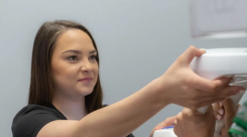 Woman in black shirt undergoing a medical or fitness assessment using a white device held by another person.
