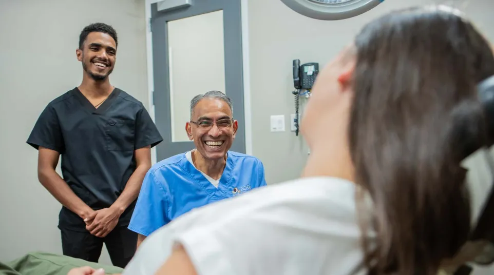 Smiling dentist and assistant talking to a female patient in a dental office, creating a friendly atmosphere