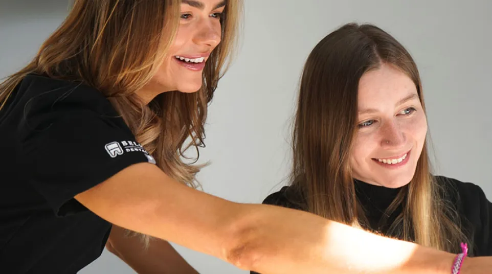 Smiling female dental professional showing a young woman something while seated in a dental clinic