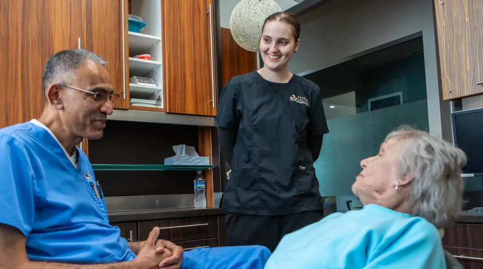 Dentist consulting elderly female patient in dental office with assistant smiling in background
