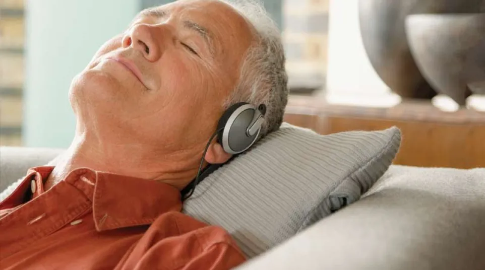 Older man relaxing on a couch with headphones on, eyes closed, enjoying music or meditation.