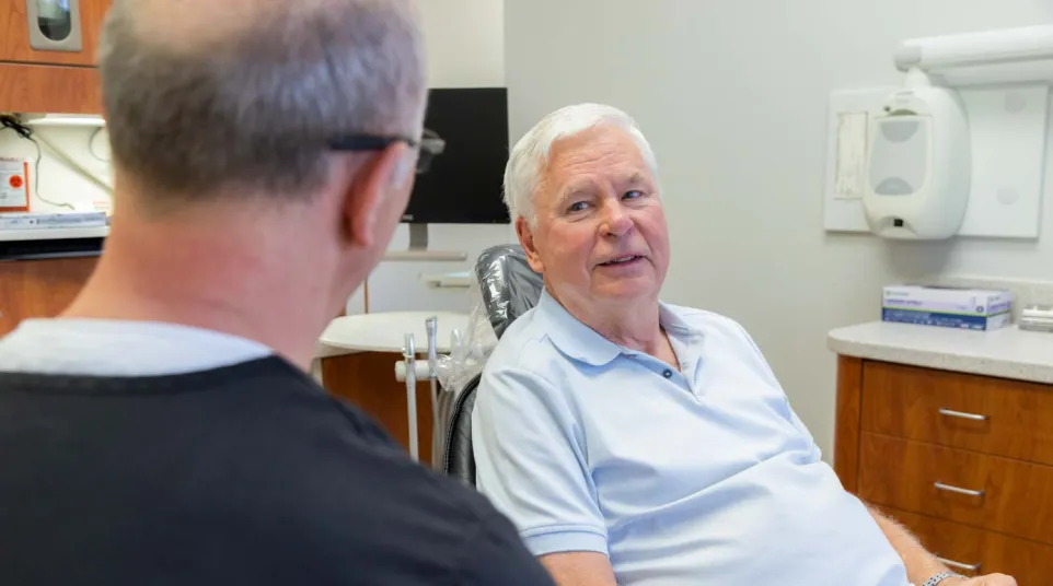 Senior man in light blue shirt consulting with dentist in a modern dental office setting.