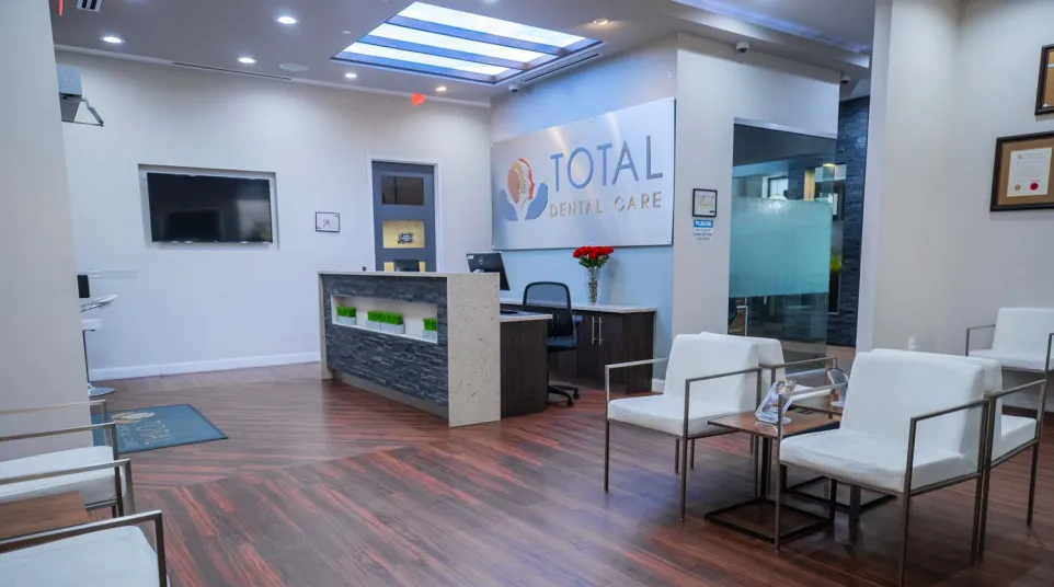 Modern dental office reception area with wooden floors, white chairs, and Total Dental Care sign on wall
