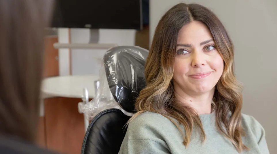 Woman with wavy hair sitting in a dental chair smiling softly during consultation with dental professional.