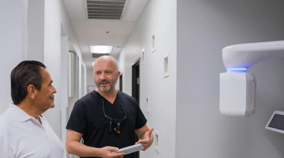 Dentist in black scrubs discussing treatment with a patient in a modern dental clinic hallway