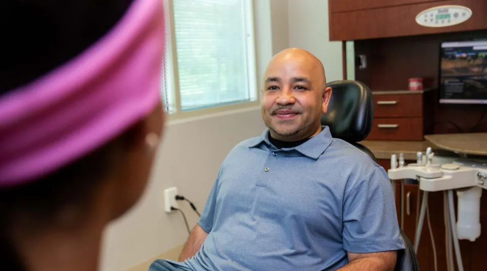 Smiling man sitting in a dental chair talking to a female dentist in a modern dental office.