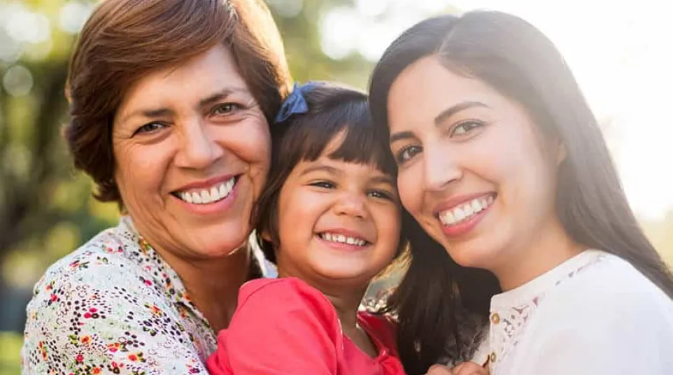 Three generations of women smiling outdoors, embracing and enjoying a sunny day together.