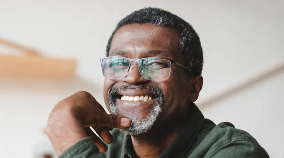 A smiling older man in glasses poses confidently, wearing a green shirt and sitting indoors.