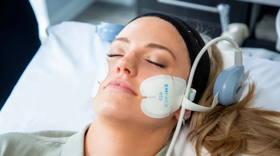 Woman resting with EMFACE facial treatment pads on cheeks undergoing skin therapy