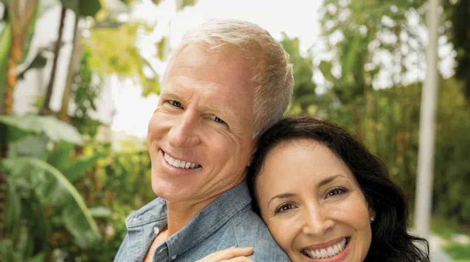 Happy middle-aged couple smiling outdoors with greenery in the background, embracing affectionately by the pool.