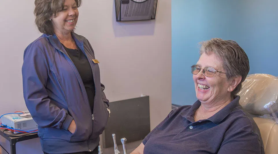 Dental hygienist reviewing patient information with smiling woman in bright orange top in modern dental office