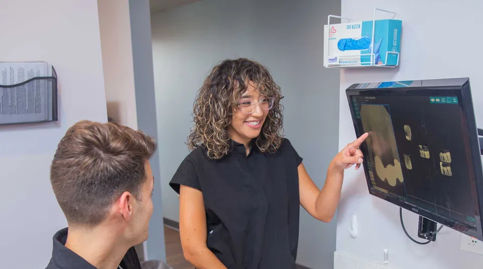 Smiling woman in orange sweater handing a card to receptionist at an office desk with computer screen visible