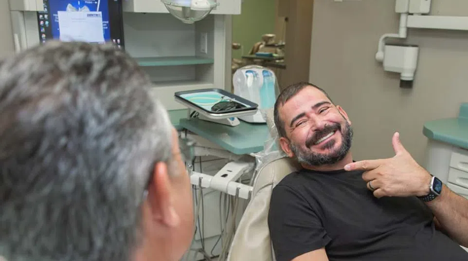 Smiling man pointing to his teeth while sitting in a dental chair during a dentist consultation session.