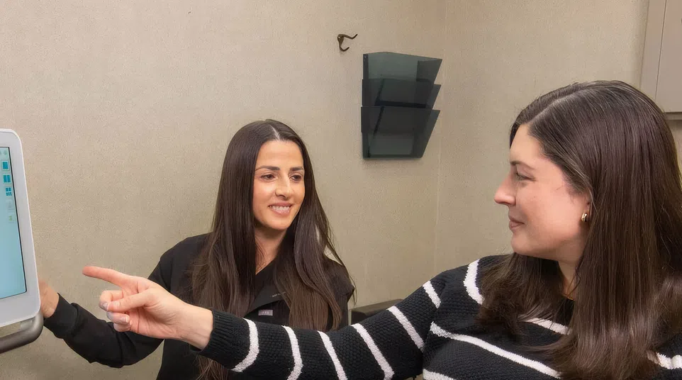 Two women in a consultation room, one pointing at a screen while the other attentively listens and smiles.