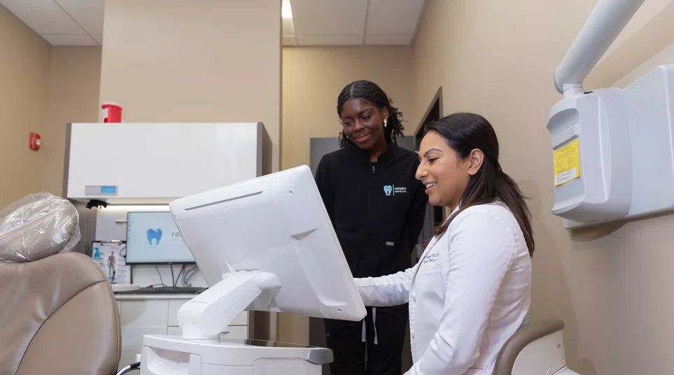 Dentist and dental assistant reviewing patient information on a computer in a modern dental office.