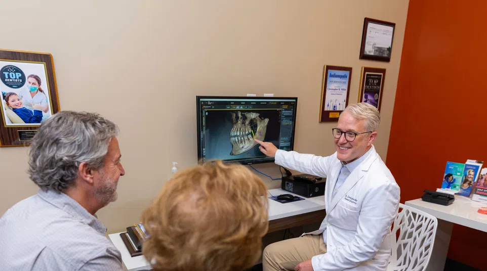 Dentist explaining dental X-ray results to a middle-aged couple in a modern consultation room.