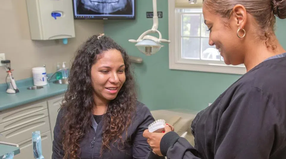 Dentist showing dental mold to patient in clinic with dental X-ray on monitor