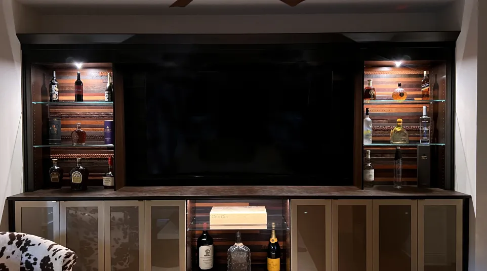 Custom designed whisky room with whisky bar and glass shelves, whisky bottles, glass cabinets, accent lighting, a large flat screen tv and a hardwood floor