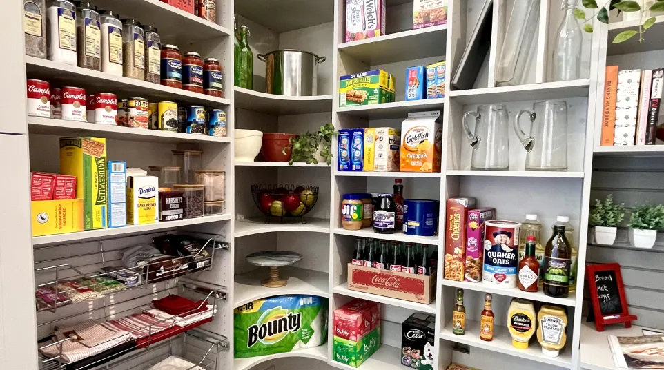 Organized kitchen pantry shelves with canned goods, snacks, paper towels, beverages and kitchen essentials