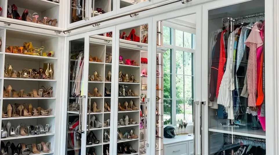 Spacious walk-in closet with mirrored doors, open shelves displaying high heeled shoes, hanging clothes and accent lighting