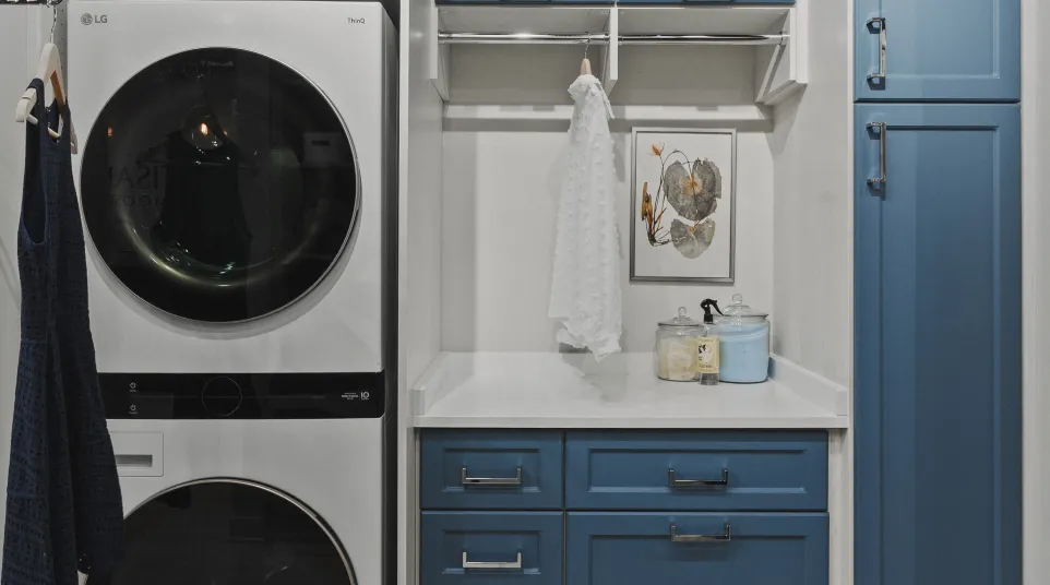 Modern laundry room with stacked LG washer and dryer, blue cabinets, white countertop, rod for hanging clothes and laundry supplies